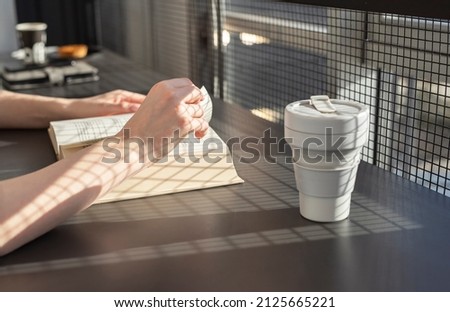 Woman sitting at cafe table with eco cup and reading book. Hands closeup flipping book pages. High quality photo