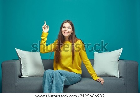 Smiling creative young girl point finger up, find answer to question, good idea, solution, feel insight sitting on couch