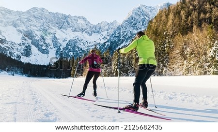 Caucasian couple moving in sync while cross country skiing on the ski trail surrounded by mountains and forest.