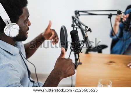Multiracial hosts streaming podcast together at studio - Focus on african man headphones