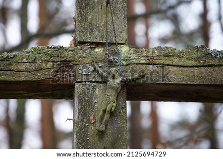 A very old wooden cemetery cross with a statue of Jesus hung on a metal chain.