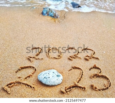 Happy New Year 2023 text on the sea beach. Handwritten inscription 2022 and 2023 on beautiful golden sand beach. Abstract background photo of coming New Year 2023 and leaving year of 2022.
