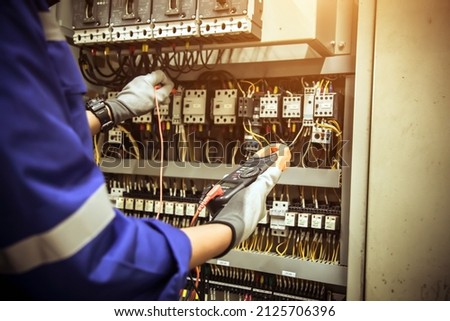 Electricity and electrical maintenance service, Engineer using measuring equipment tool checking electric current voltage at circuit breaker terminal and cable wiring main power distribution board. Royalty-Free Stock Photo #2125706396