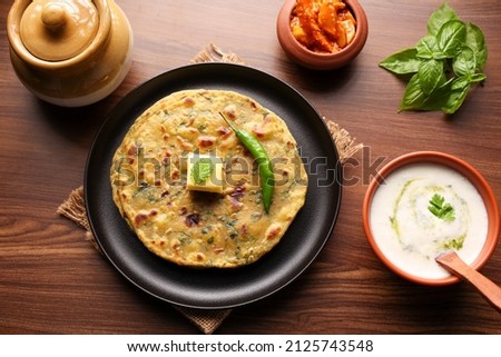 Palak paratha butter on spinach paratha , parantha ,chapati Indian flatbread roti made from spinach served in golden plate with yogurt mint dip, mango pickle, North Indian breakfast food Delhi India. Royalty-Free Stock Photo #2125743548