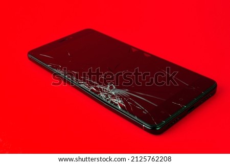 A mobile phone with a broken screen lies on a red background. A broken smartphone. Electronic gadget in need of repair. Horizontal image.