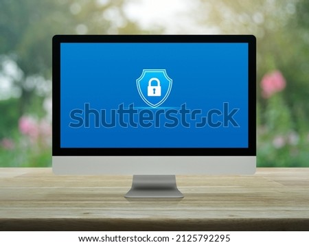 Padlock with shield flat icon on desktop modern computer monitor screen on wooden table over blur pink flower and tree in park, Technology security insurance online concept