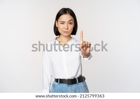 No. Young serious and confident asian woman showing stop, one finger gesture, taboo sign, standing over white background Royalty-Free Stock Photo #2125799363