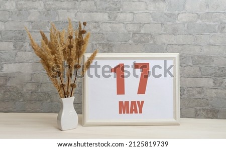 may 17. 17th day of month, calendar date.  White vase with ikebana and photo frame with numbers on desktop, opposite brick wall. Concept of day of year, time planner, spring month.