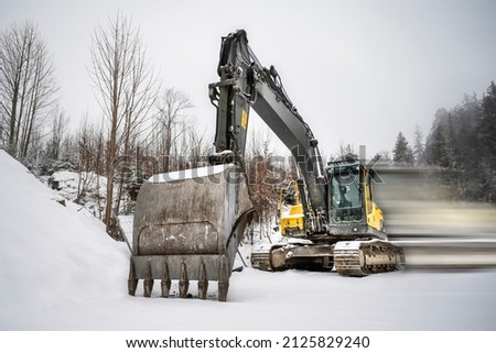 Construction site crawler excavator stands in a winter landscape with motion blur and a large shovel