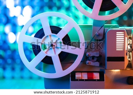 Retro reel with film rotating on colorful shining sparkles wall. Old-fashioned 8mm film projector playing in glitter room. Vintage objects, Oscar, cinema, Hollywood concept