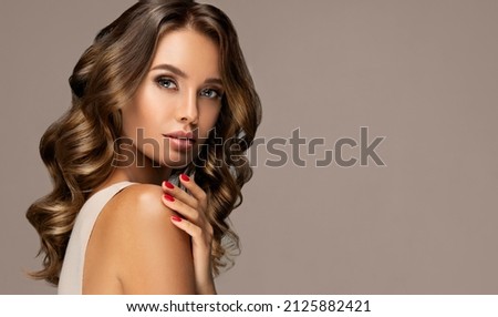 Beautiful woman  with long  and   shiny wavy  hair .  Beauty  model girl with curly hairstyle and red manicure nails  Royalty-Free Stock Photo #2125882421