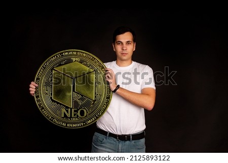 A man holds a NEO coin in his hands as a symbol of technology. Image on black background