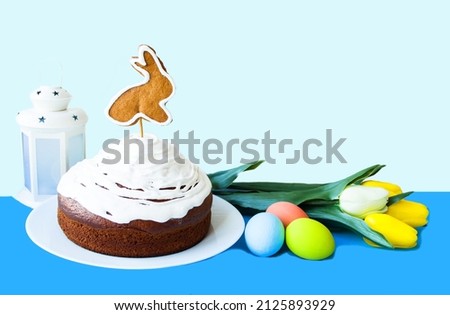 Concept spring holiday bright easter.  On a blue background, an Easter cake decorated with cookies, a figurine of a rabbit in the tradition of Easter.  Multi-colored eggs and spring flowers tulips.
