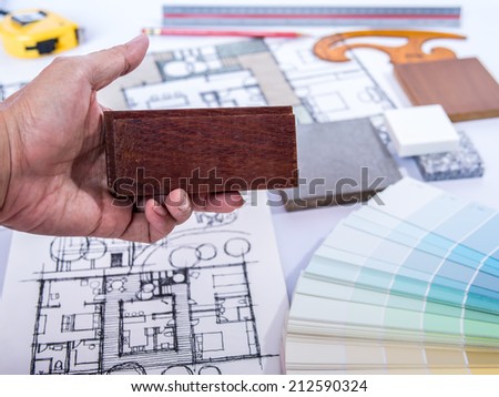 Architect's hand holding wood sample for  home renovation project with drawing