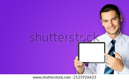 Happy smiling businessman in white shirt and tie, showing pointing finger tablet pc touchpad, ipad with copy space, mock up screen over violet purple background. Confident business man at studio image