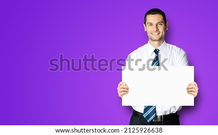Happy smiling businessman in white shirt and tie, showing blank mockup mock up signboard with copy space area for text, violet purple background. Confident business man holding paper board at studio.