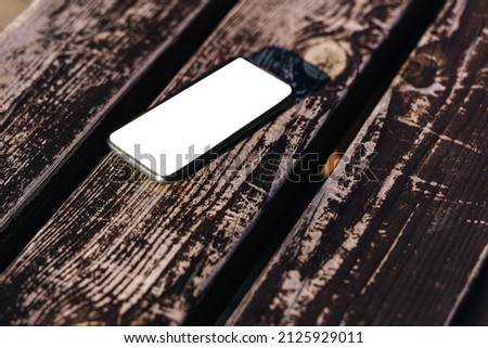 Mockup phone with a white screen lies on the background of a dilapidated wooden bench.