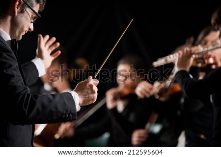 Conductor directing symphony orchestra with performers on background. Royalty-Free Stock Photo #212595604