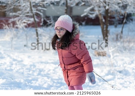 A small child in warm clothes and a knitted hat pulls a sled by a rope on the rolled snow. Photo shoot on a beautiful sunny day outdoors