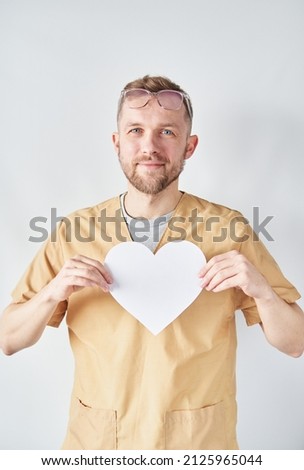 Portrait of a professional male caucasian doctor or nurse wearing eyeglasses with white paper heart shape. Medical and healthcare or National Doctor's Day concept. High quality vertical photo