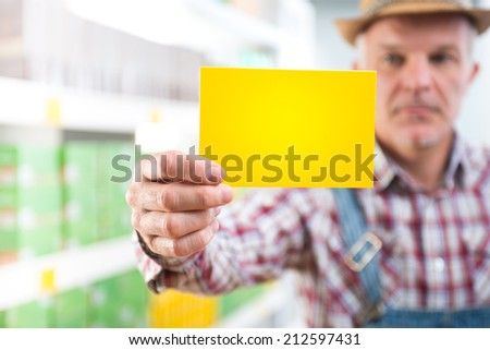Farmer in checked shirt and dungarees holding a sign at supermarket.