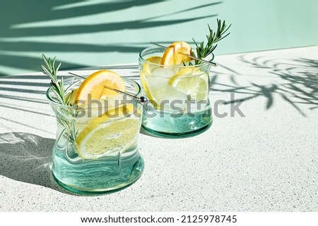 Summer refreshing lemonade drink or alcoholic cocktail with ice, rosemary and lemon slices on pastel light green surface. Fresh healthy cold lemon beverage. Water with lemon. Royalty-Free Stock Photo #2125978745