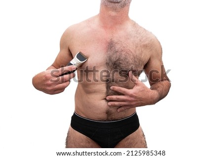An athletic older Caucasian man, bare chested hairy, holding a razor in his hand, half shaved chest. Isolated on white background.