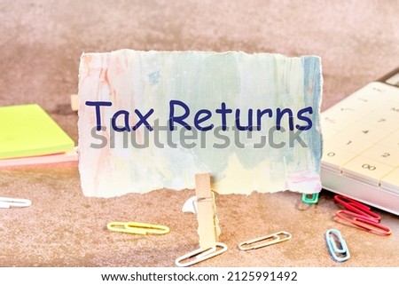 tax returns text written on paper next to scattered paper clips, calculator, adhesive paper.