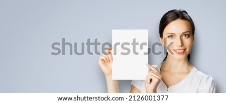 Studio portrait image of cheerful smiling woman in white cloth, holding showing demonstrate mock up paper signboard. Business and advertising concept. Copy space empty free area for text. Grey color.