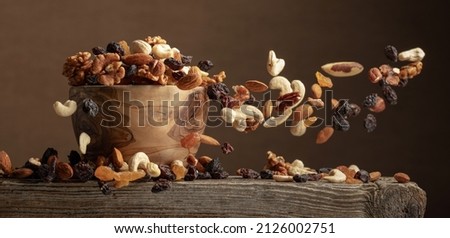 Flying dried fruits and nuts. The mix of nuts and raisins in a wooden bowl. Royalty-Free Stock Photo #2126002751