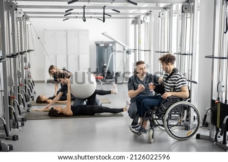 People doing exercises at rehabilitation center. Worker helps a guy in a wheelchair to do exercises for recovery from injury Royalty-Free Stock Photo #2126022596