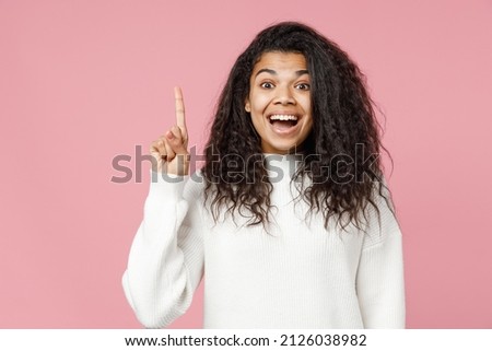 Young insighted happy smiling african american woman 20s curly hair in white knitted sweater look camera hold index finger up with great new idea isolated on pastel pink background studio portrait