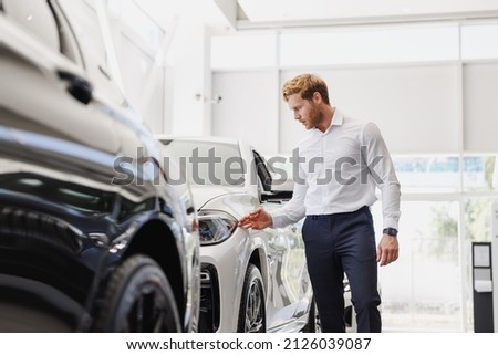 Man adult customer male buyer client wears classic suit white shirt chooses auto wants to buy new automobile touch check car in showroom vehicle salon dealership store motor show indoor. Sales concept Royalty-Free Stock Photo #2126039087