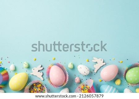 Top view photo of easter decorations easter bunnies multicolored easter eggs in paper baking molds and confectionery topping on isolated pastel blue background with copyspace