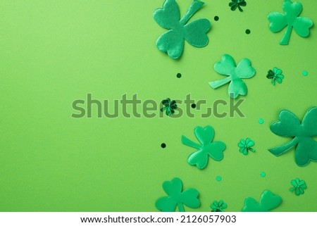 Top view photo of st patrick's day decorations green shamrocks and clover shaped confetti on isolated pastel green background with empty space
