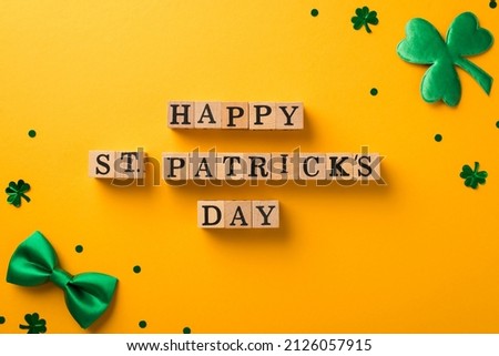 Top view photo of wooden cubes labeled happy st patricks day trefoil shaped confetti and green bow-tie in the corners on isolated yellow background