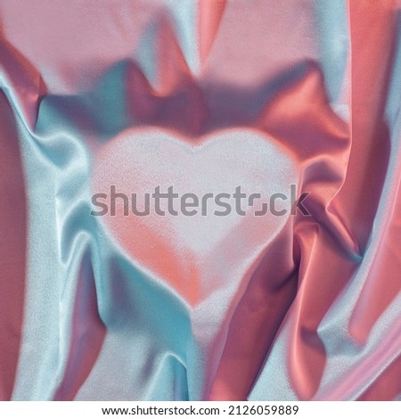 Shape of heart under a soft satin fabric with red and blue neon lights. Romantic, square background with the 70s vibes.