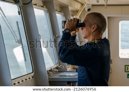 Deck officer with binoculars on navigational bridge. Seaman on board of vessel. Commercial shipping. Passenger ship. Royalty-Free Stock Photo #2126076956