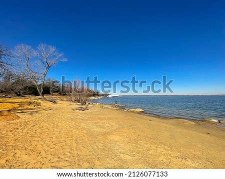 Beautiful sandy shoreline of Lake Lewisville with row of fishing rods in wintertime in a sunny clear blue sky day. Recreation lake and reservoir near Dallas, Texas, America Royalty-Free Stock Photo #2126077133