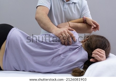 A chiropractor palpates the area of the scapula on the back of the patient. Appointment with an osteopath. The girl lies on the couch, the doctor works with her back. Back view Royalty-Free Stock Photo #2126081903