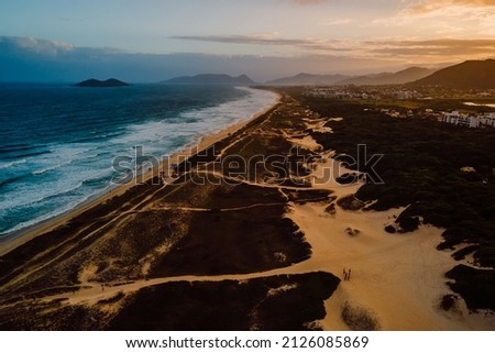 Beach with dunes, ocean and town with sunset lights in Campeche, Florianopolis
