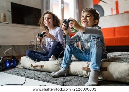 Two children small caucasian brother and sister happy children siblings boy and girl playing video game console using joystick or controller while sitting at home real people family leisure concept Royalty-Free Stock Photo #2126090801