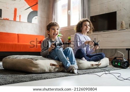 Two children small caucasian brother and sister happy children siblings boy and girl playing video game console using joystick or controller while sitting at home real people family leisure concept Royalty-Free Stock Photo #2126090804