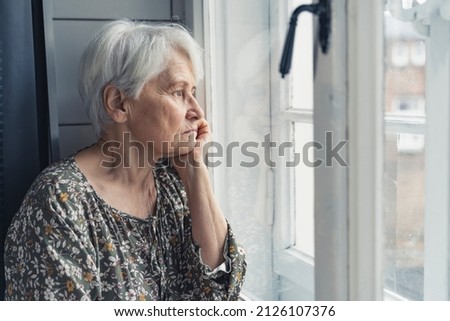 portrait of a sad grandma sitting all alone during Mother's Day and looking out of the window. High quality photo Royalty-Free Stock Photo #2126107376