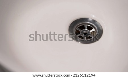 Streaming water in white sink. Closeup flow pour to drain hole in bathroom or kitchen.