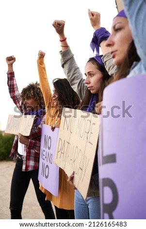 Vertical photo of a group of women marching on the road in protest. Young woman holding a protest sign about women empowerment.