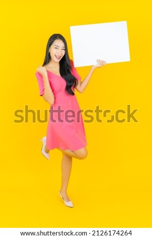 Portrait beautiful young asian woman smile with empty white billboard on yellow background