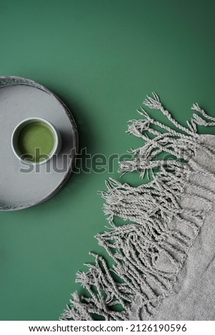 A cup of matcha tea and a rug on a jade green background. Monochrome, modern, top view. 