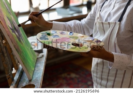 Close up cropped young male artist holding palette with mixed acrylic paints, involved in creating artwork on canvas, improving art painting skills, enjoying hobby activity in modern studio or home. Royalty-Free Stock Photo #2126195696