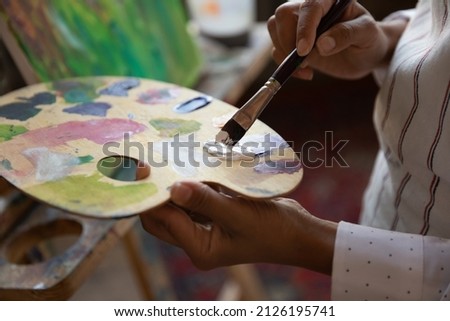 Close up focus on palette with mixed paints, motivated young professional artist drawing new artwork on canvas, creating colors, improving craft skills or enjoying master class in gallery or studio.